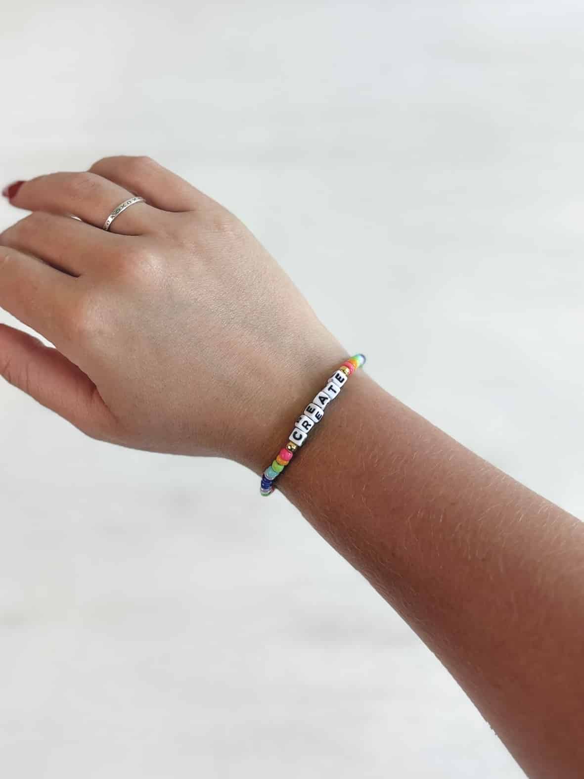 Colorful beaded bracelet spelling CREATE in block letters, worn on wrist.