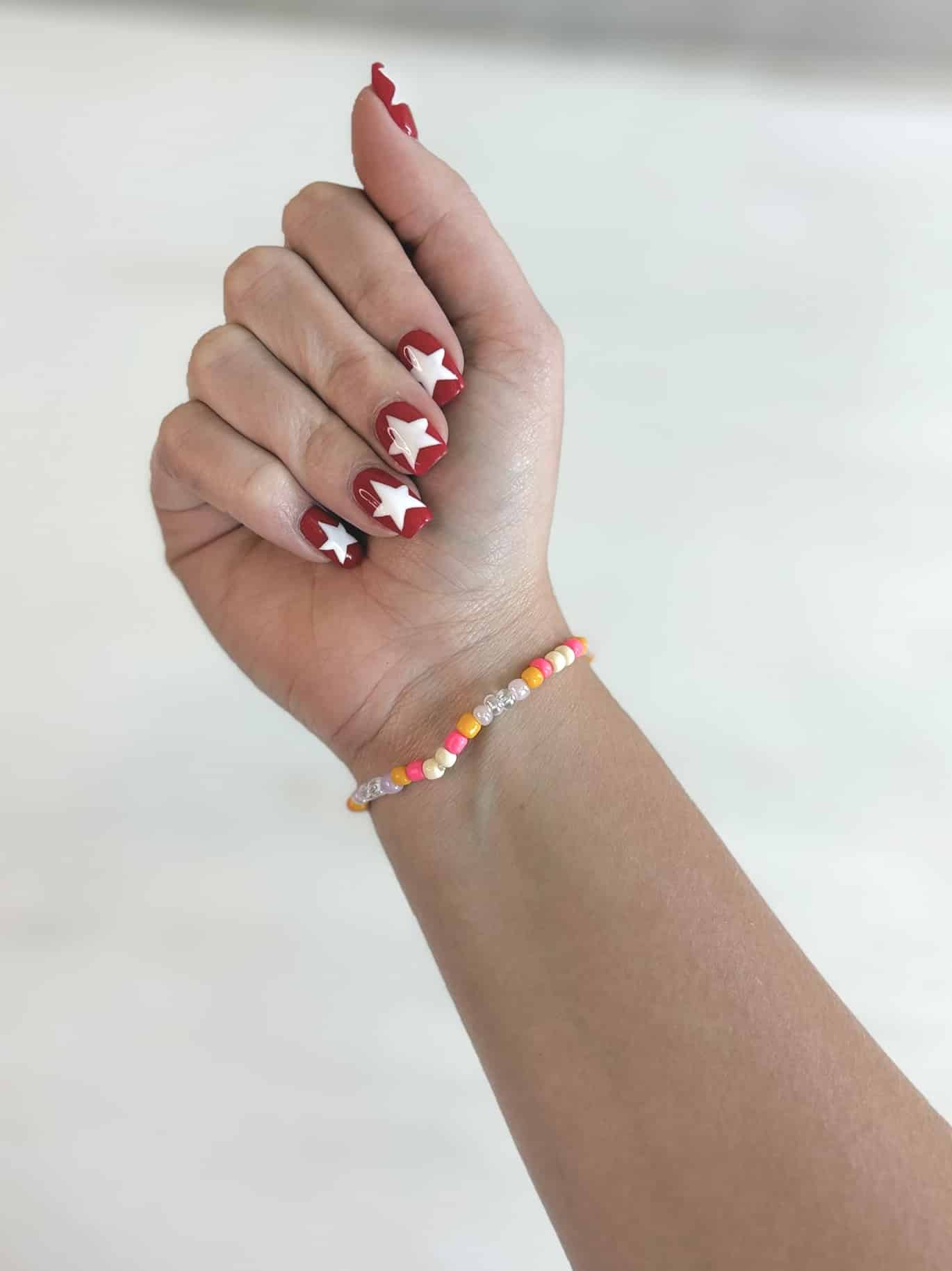 Bookish friendship bracelet shown on wrist with red and white star nail art.