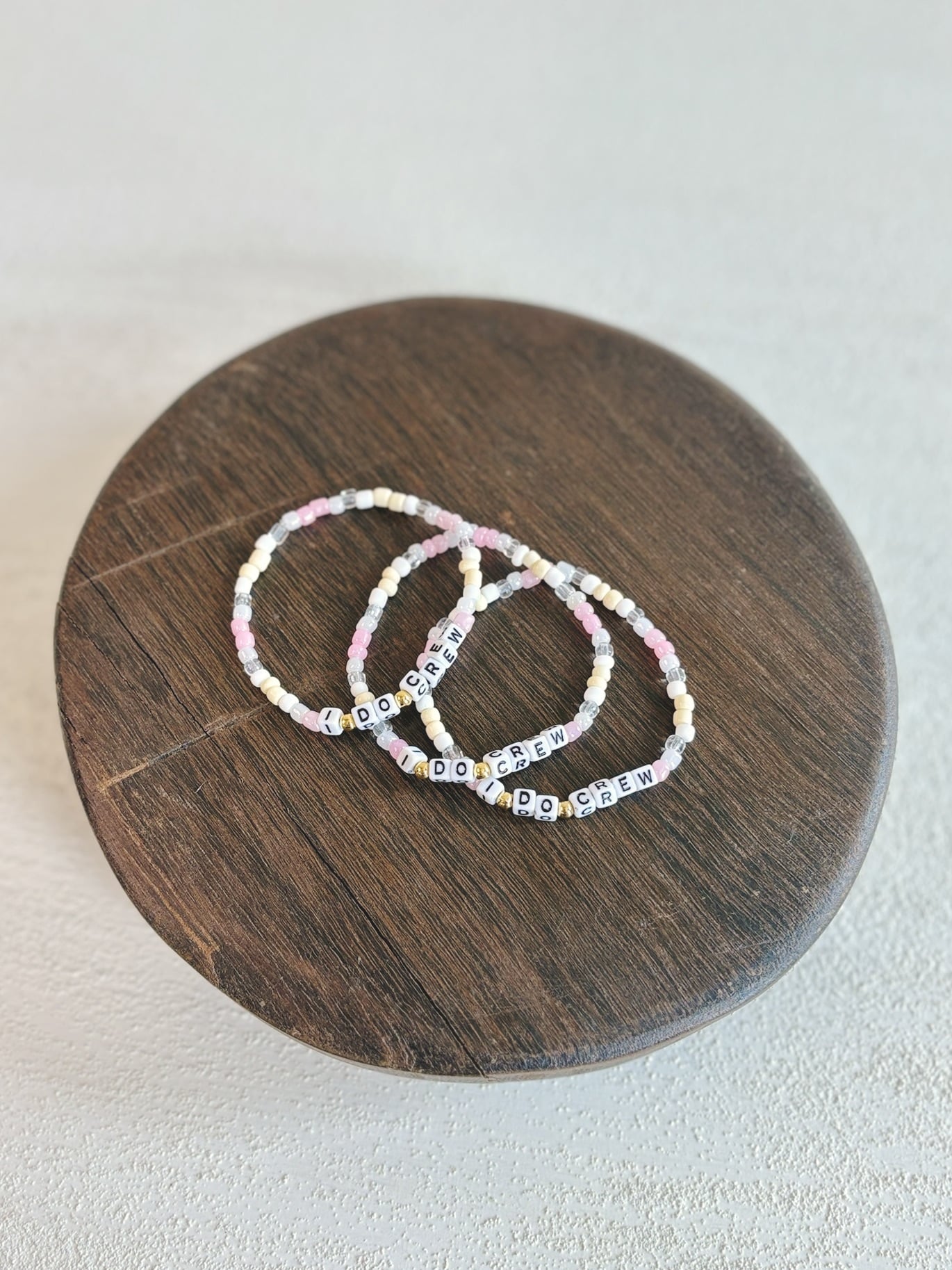 I Do Crew bridal party beaded bracelets displayed on a small, rustic found wood pedestal with rich grain and handcrafted texture.