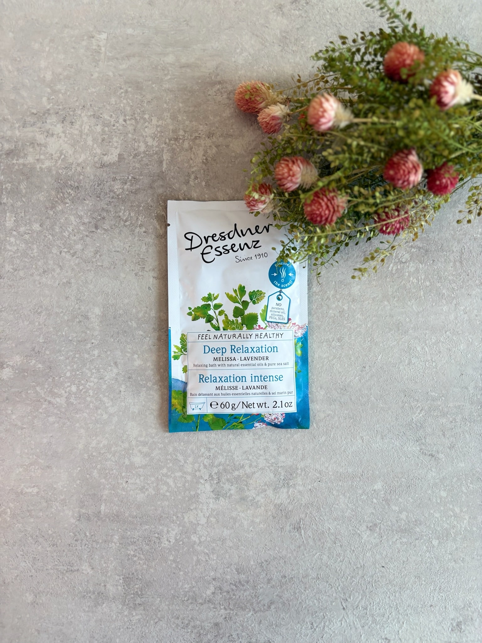 Deep Relaxation Bath Salt by Dresdner Essenz styled with pink blooms on a gray tabletop.