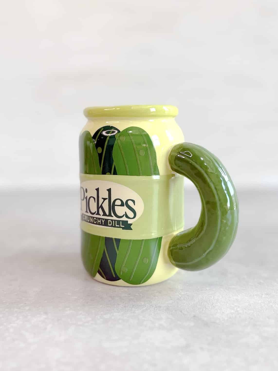 Side angle of the pickle-themed ceramic mug with handle on the left and pickle illustrations wrapped around.