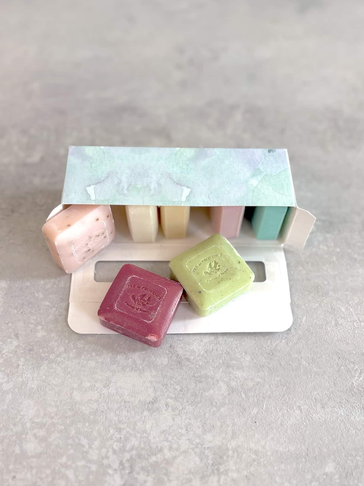 Open floral box of mini French soaps with two bars pulled out in front.