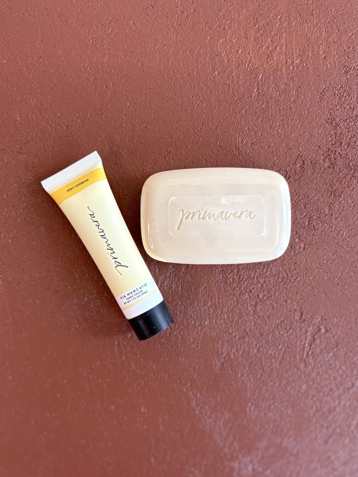 Unboxed Mint Verbena bar soap and hand cream displayed on terracotta surface.