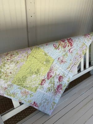 Flower Market Quilt Throw Blanket draped over a white bench, showcasing its full pastel floral patchwork.