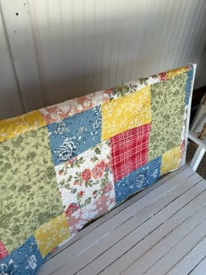 Detailed view of the Floral Quilt Farmhouse Throw Blanket showing yellow, green, blue, and floral print patches.