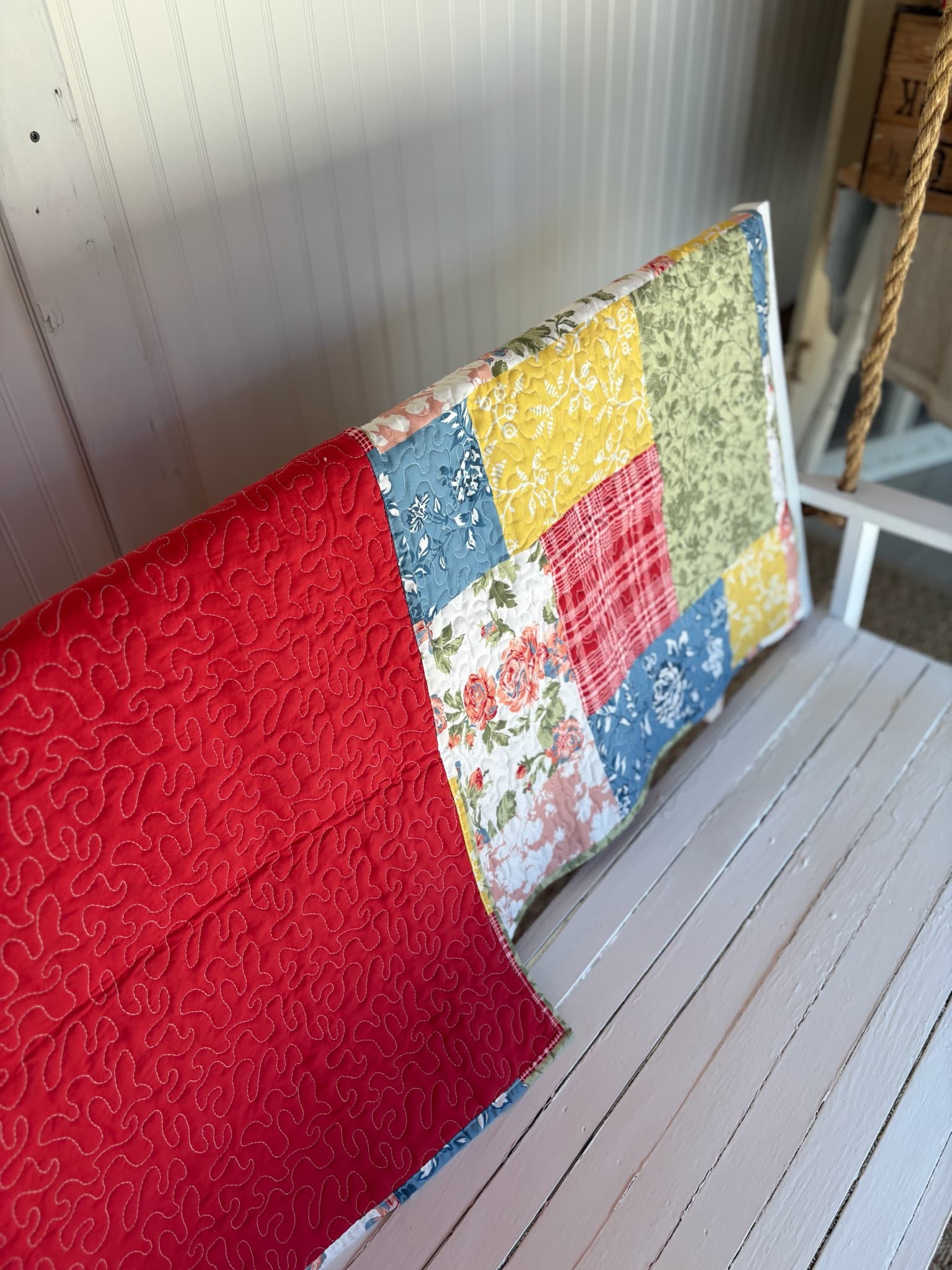 Floral Quilt Farmhouse Throw Blanket draped over a bench, showing the full patchwork front and solid red quilted back.