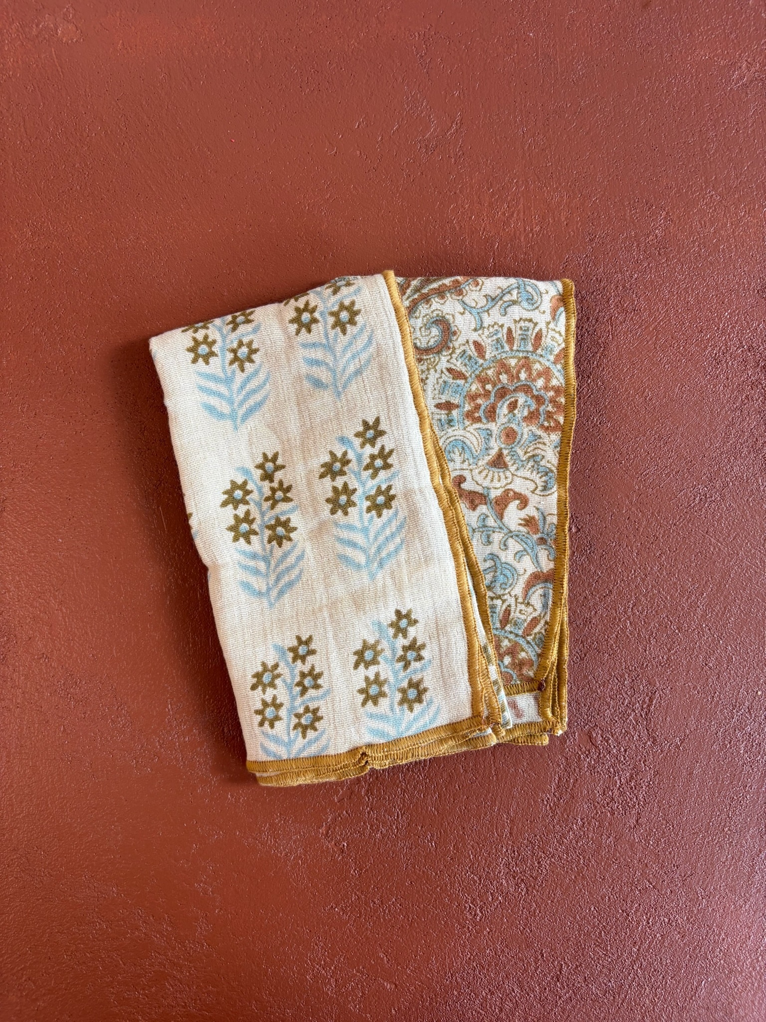 Amber Floral Kitchen Towel Set folded and displayed flat on a terracotta background, showing both the floral and block print patterns.