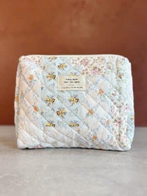 Front-facing view of the medium quilted floral makeup bag with stitched label reading “today, mood feel the warm.”