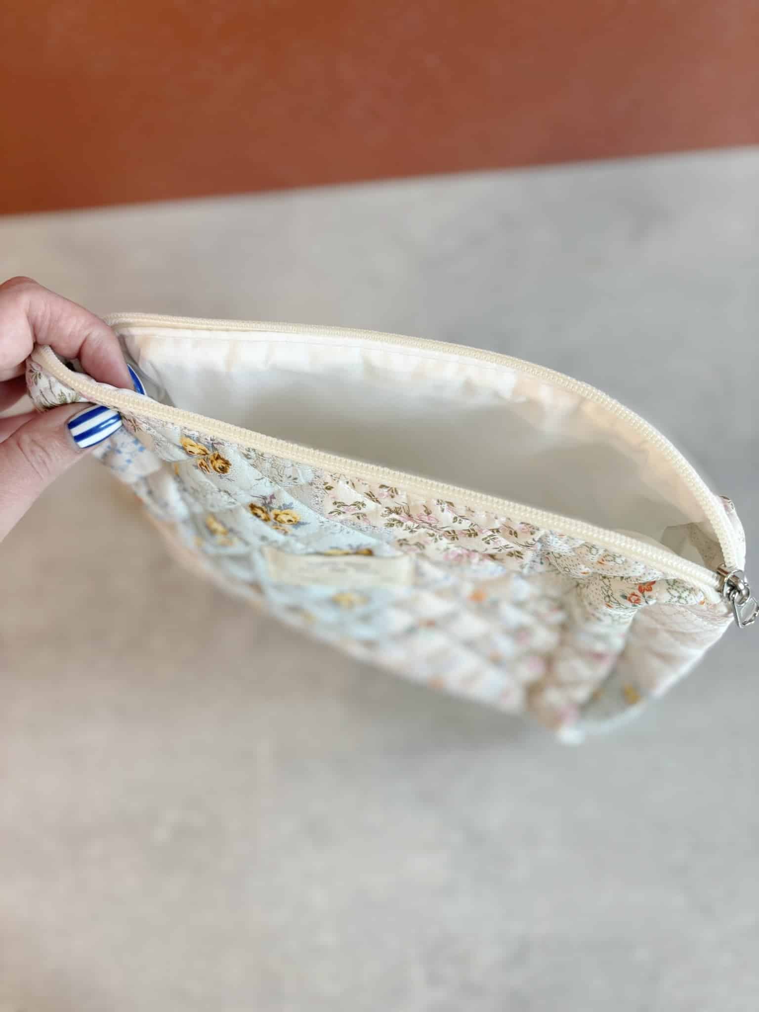 Side view of the medium floral quilted makeup bag with the zipper open, revealing spacious, wipeable interior.
