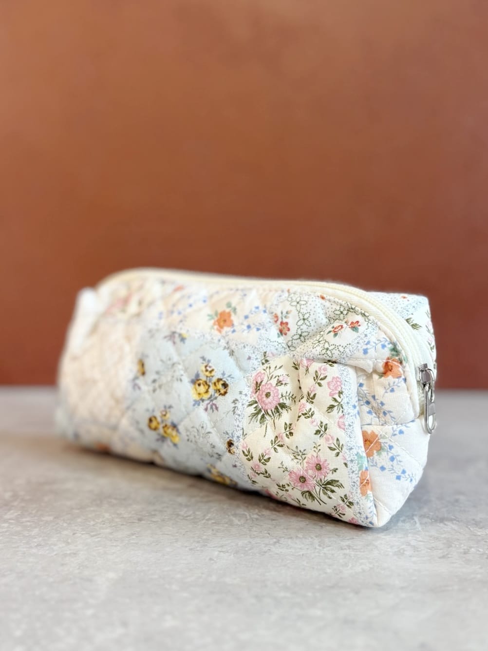 Angled view of the small floral quilted pouch showing zipper closure and soft structure on a neutral surface.