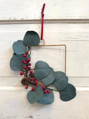 Mini square Christmas wreath with eucalyptus, red berries, and pinecones on a gold metal frame.