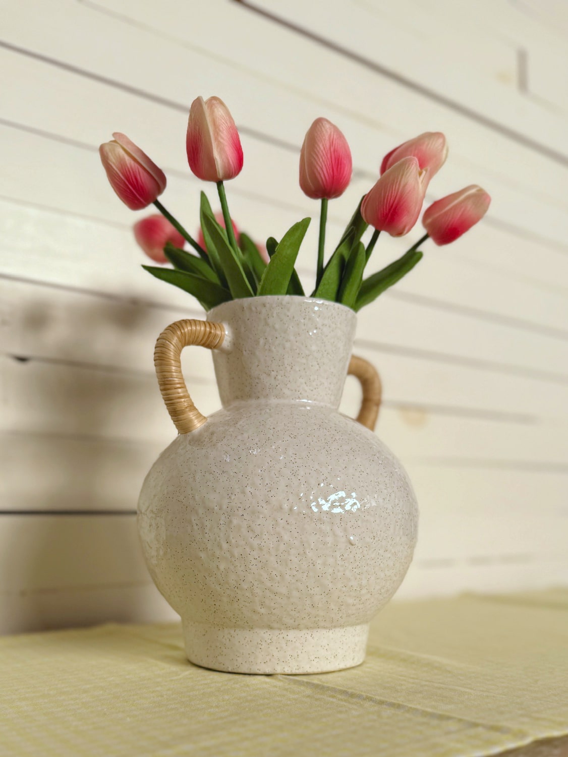 Bright Pink Tulip Bundle styled in the Rattan Wrapped Handle Vase Medium on a yellow table runner with glass candle holders.
