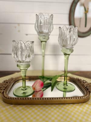 Mixed-height tulip glass votive holders displayed on a beaded mirror tray with tulip stem.