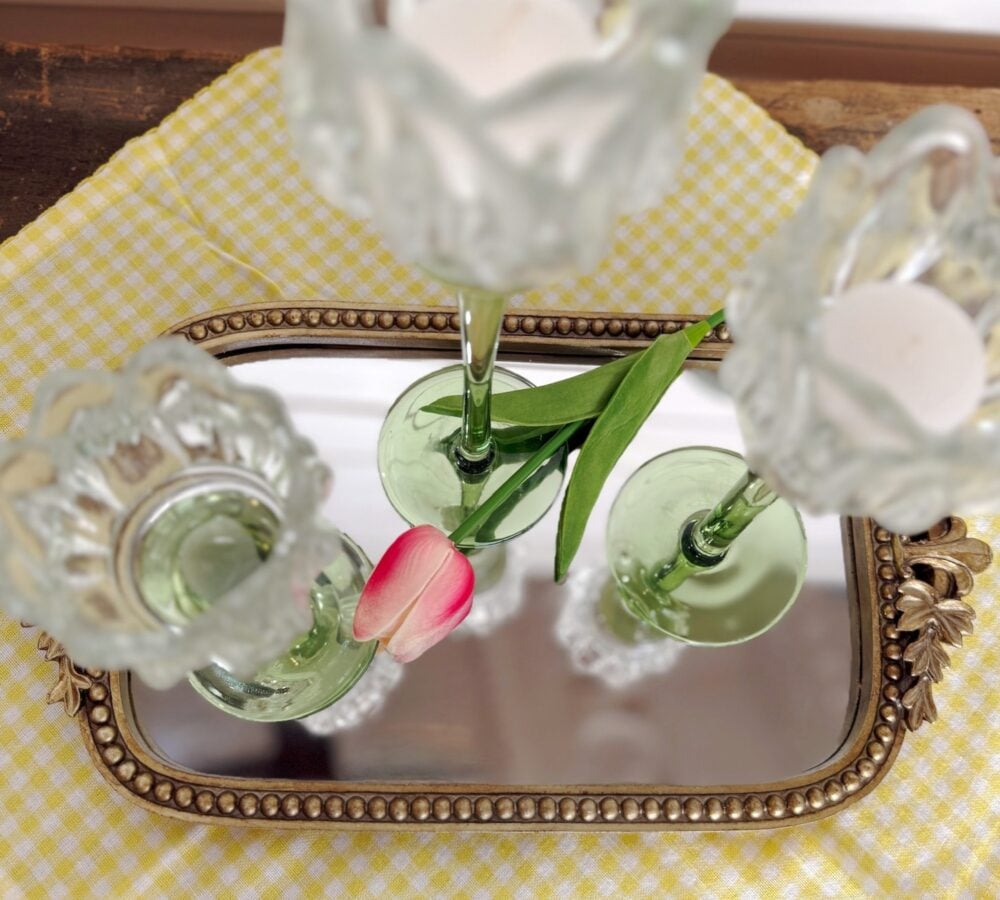 be-made-hays-ks-tulip-glass-votive-holders-beaded-gold-tray-yellow-gingham-styled-centerpiece Tulip glass votive candle holders styled on a beaded gold mirror tray with a bright pink tulip stem over a yellow gingham table runner