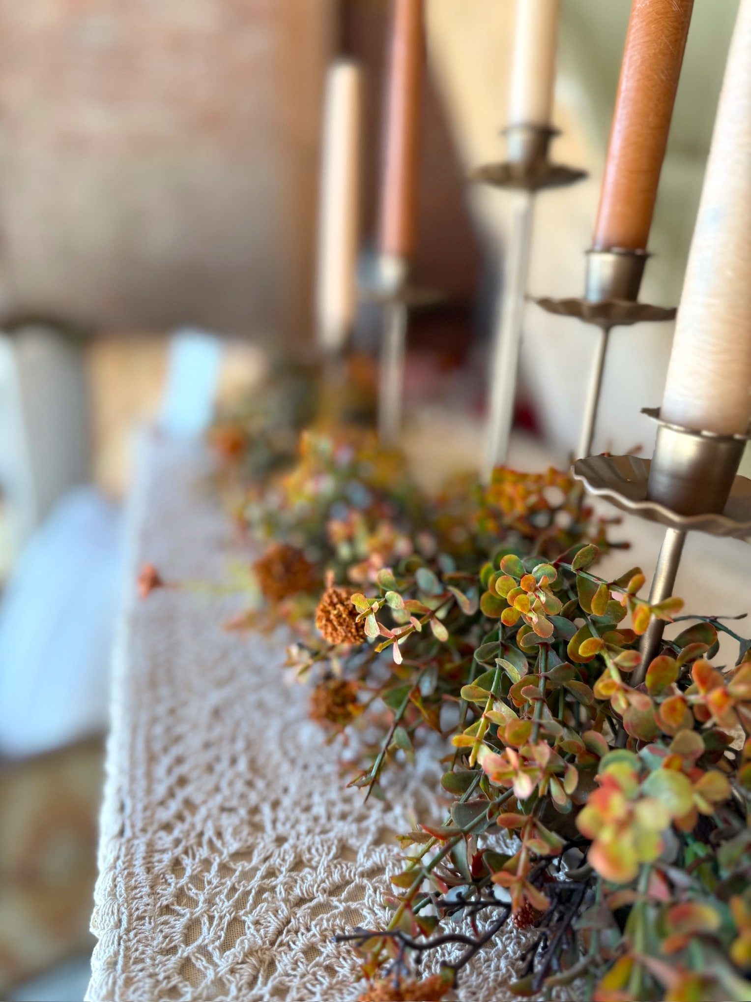Close-up of the Orange Pincushion Garland styled on a lace-covered mantel with warm taper candles.