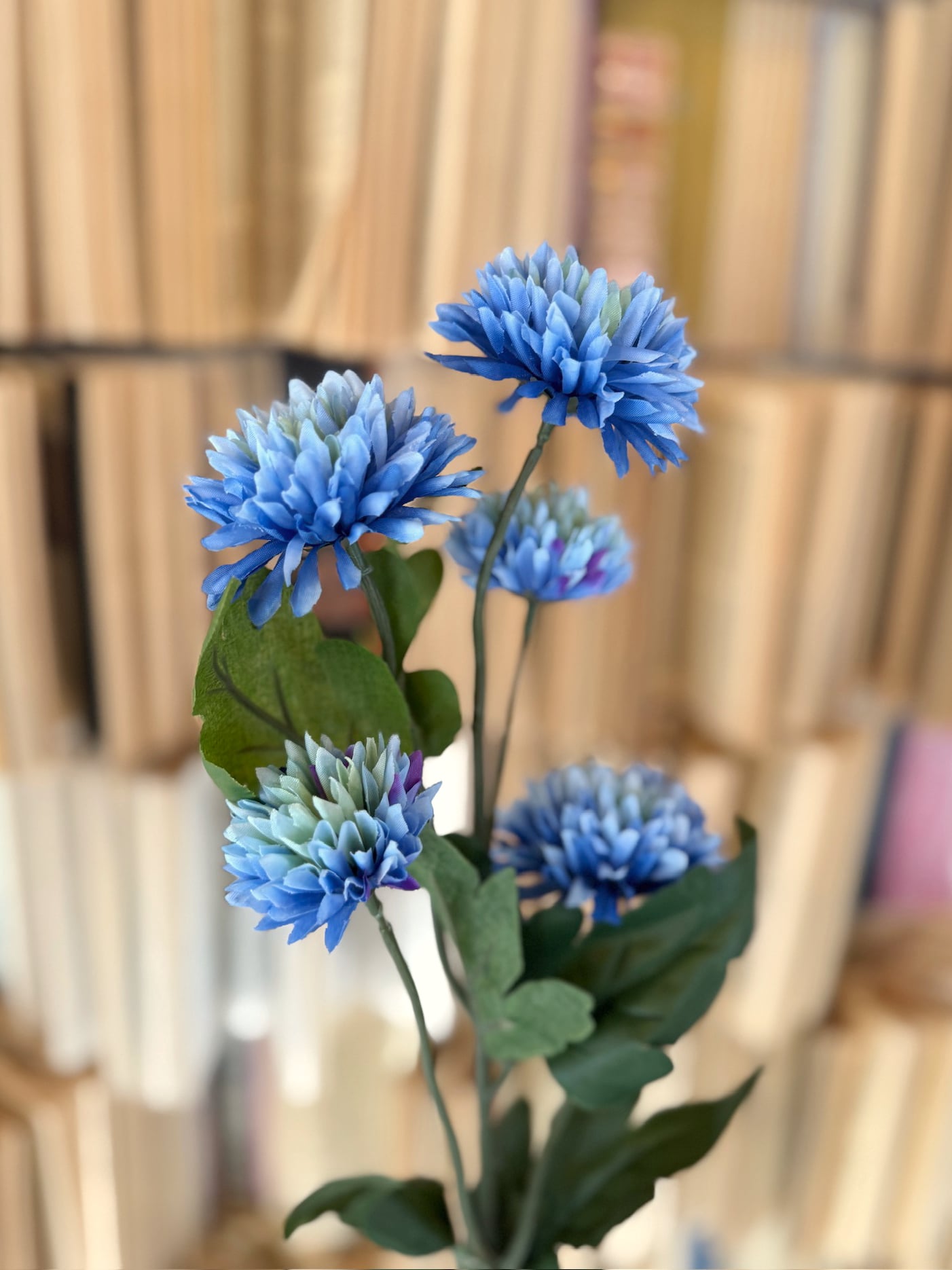 Close-up of blue mum blooms showing layered petals and dimensional texture on a faux floral stem.