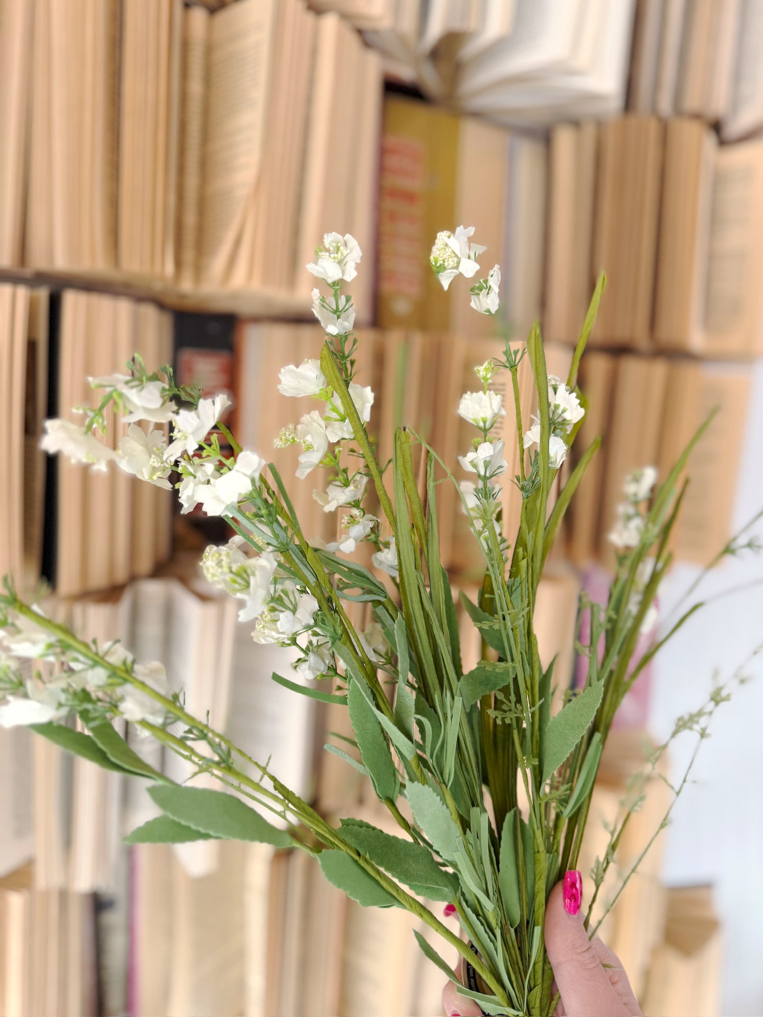 Cream Wild Flower & Grass Bush held in hand in front of vintage stacked books, featuring delicate cream blooms and wispy greenery.