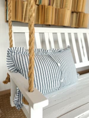 Blue stripe ruffle throw pillow styled on a white rope swing bench.