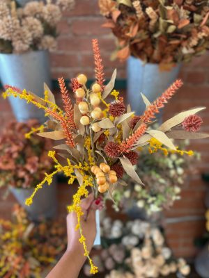 Mixed Fall Floral Pick with orange spikes, yellow blooms, and berries held in front of a floral wall display