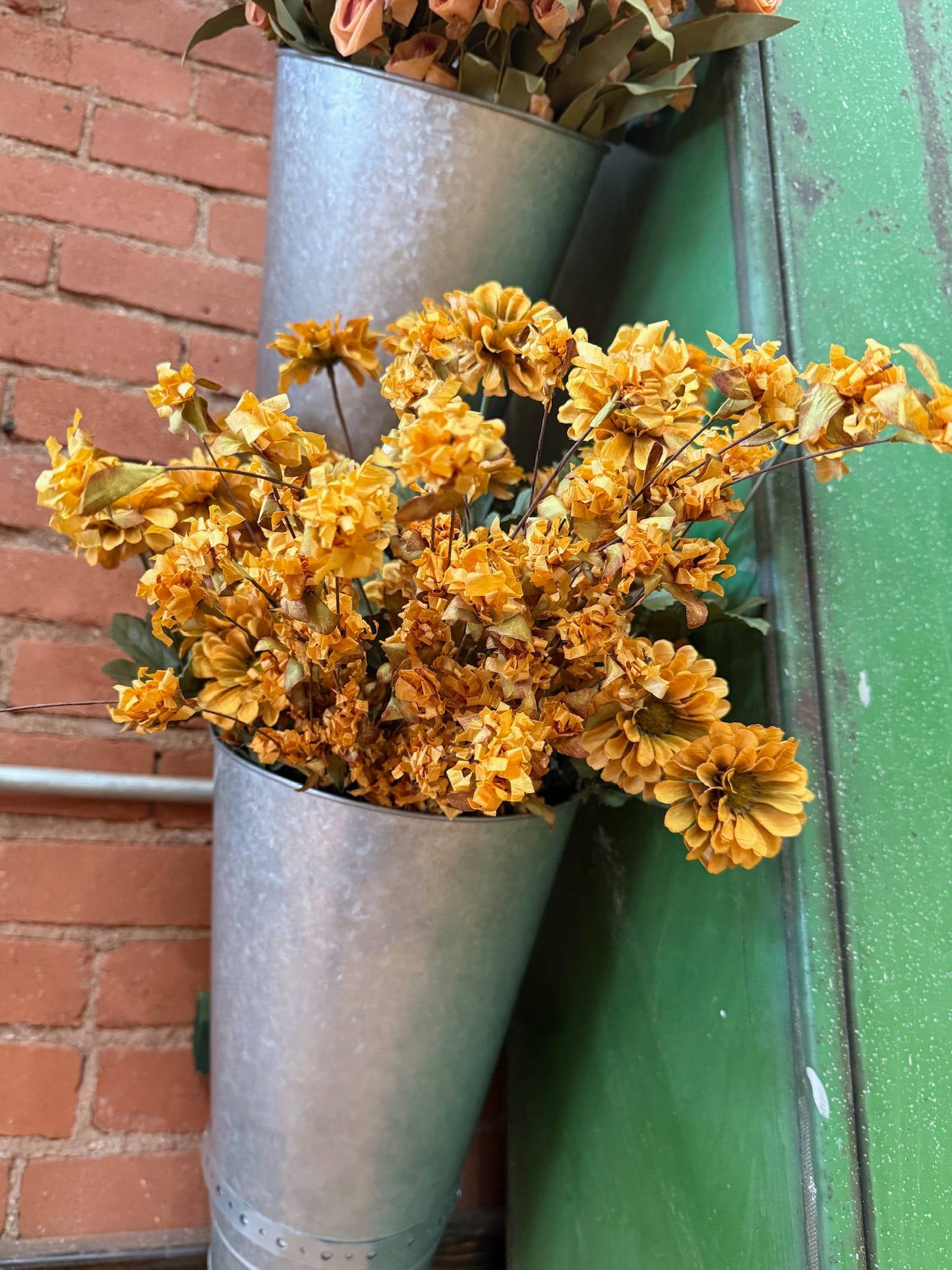 Tangerine Wild Mum Bush styled in a galvanized wall cone, surrounded by rustic brick and green wood tones.