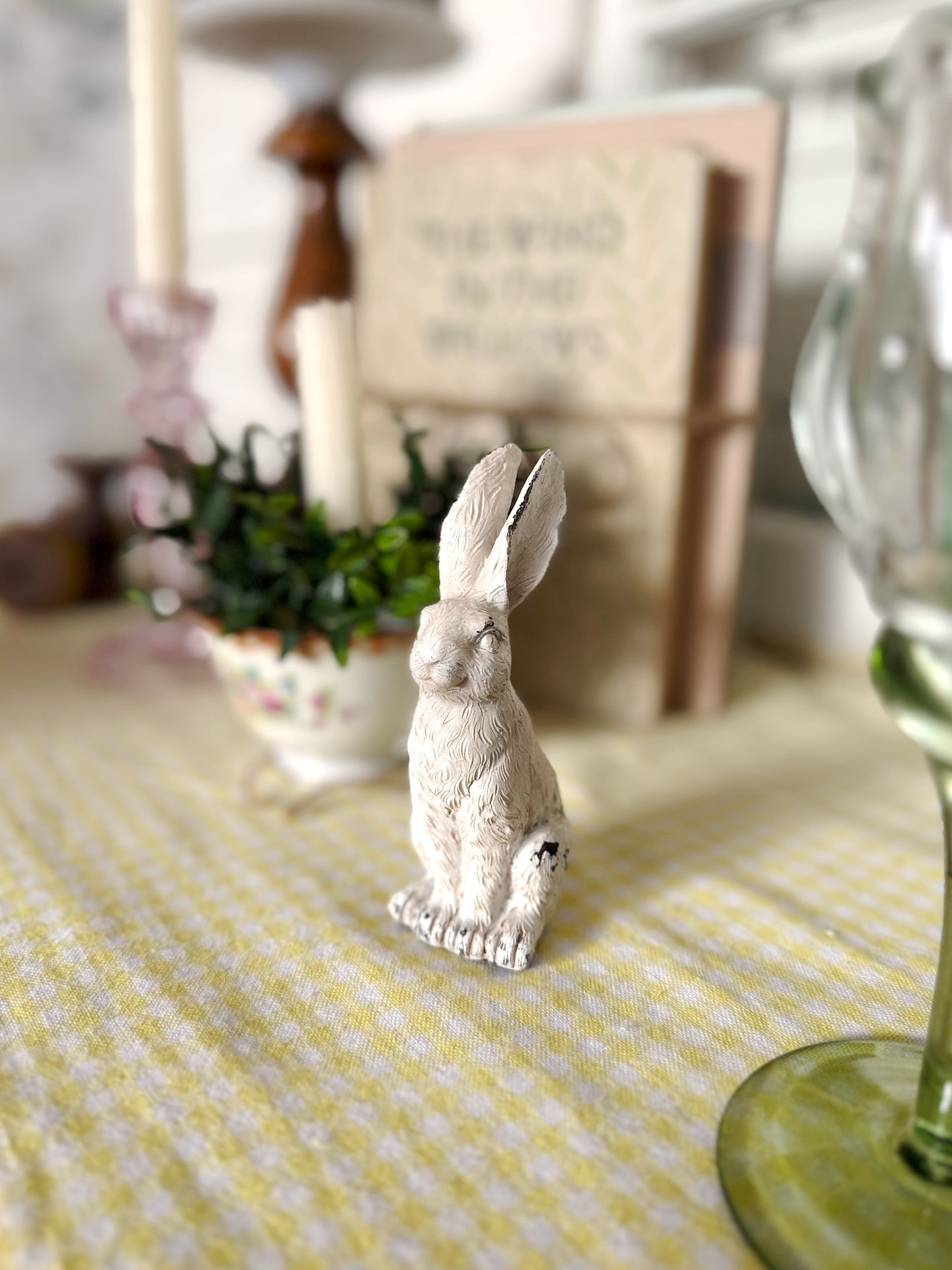 Distressed white bunny figurine styled on a soft yellow table runner with layered vintage accents.