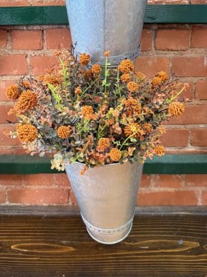 Orange Pincushion Pick styled in a galvanized metal wall vase against a brick wall