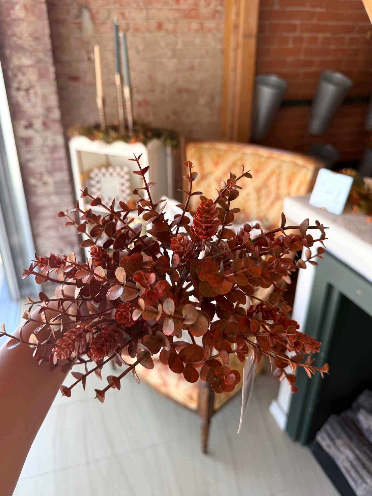 Close-up of faux orange eucalyptus and hops orb held in hand, with warm-toned fall decor in the background.