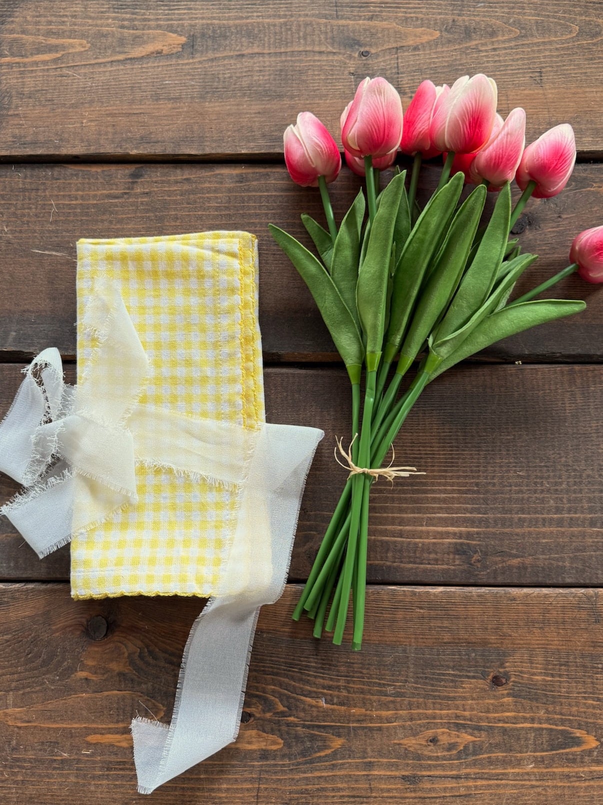 Flat lay of bright pink tulips next to a folded yellow gingham wrap with chiffon ribbon