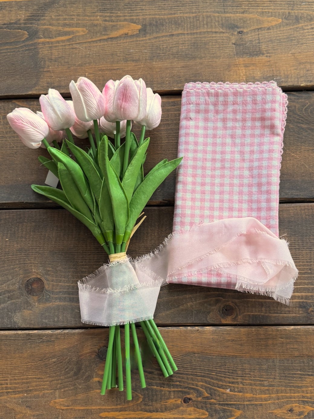 Flat lay of light pink tulips with a folded pink gingham wrap and ribbon