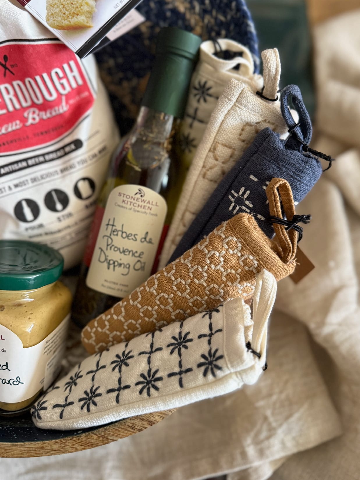 Assorted cotton pot handle covers in navy, tan, and white displayed with pantry goods and cooking accessories in a cozy kitchen setup.