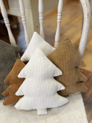 Large White Corduroy Stuffed Tree Pillows surrounded by camel and evergreen corduroy trees, adding soft neutral texture to a cozy holiday display.