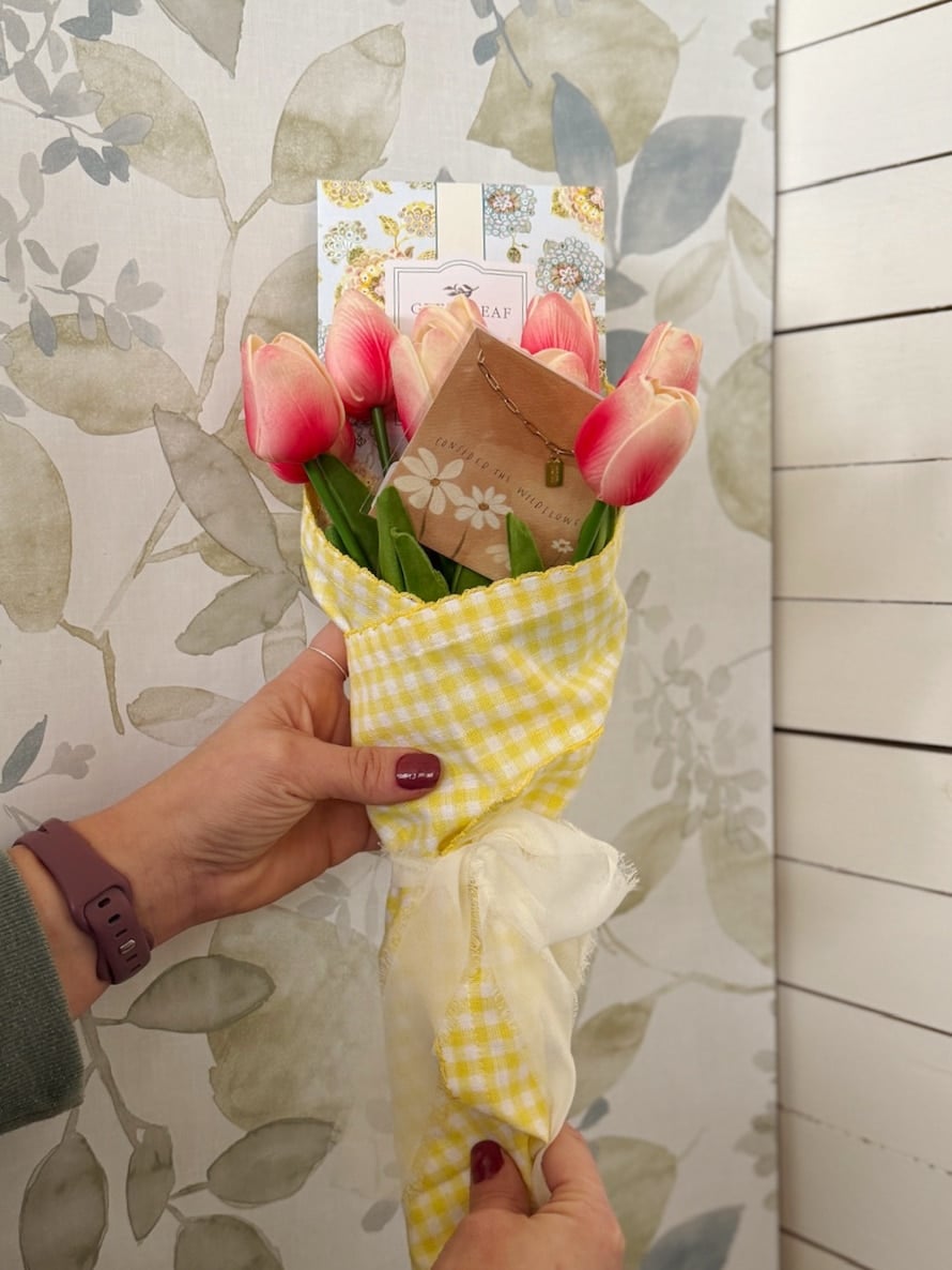 Bright pink tulip bouquet wrapped in yellow gingham fabric with gift items arranged inside