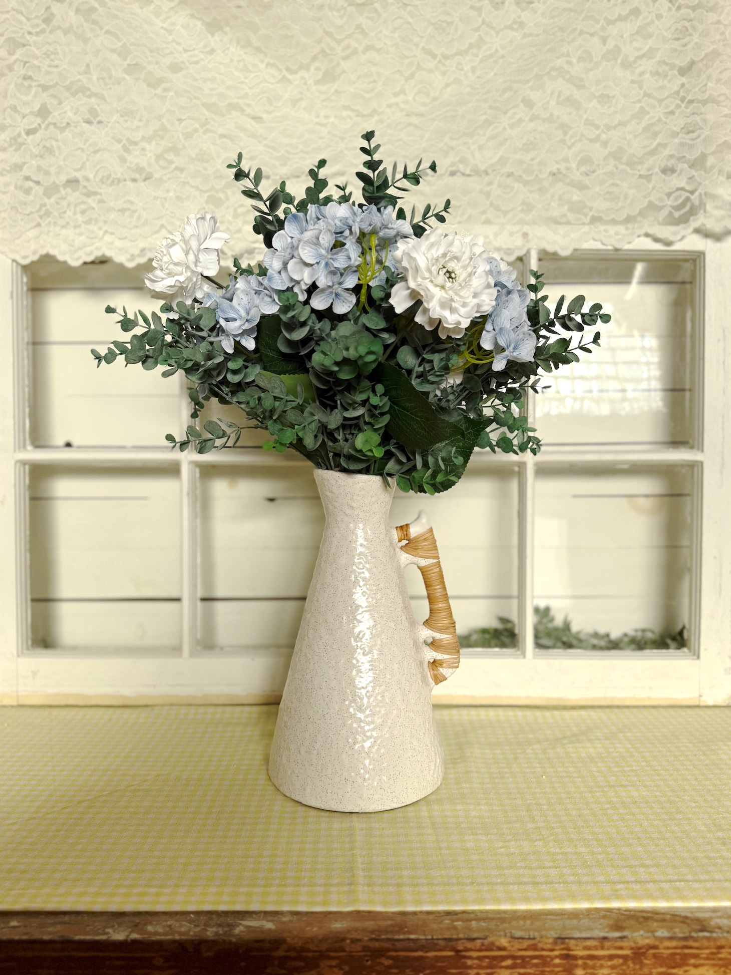 Rounded off-white ceramic vase with artisan rattan handles used as a tall centerpiece