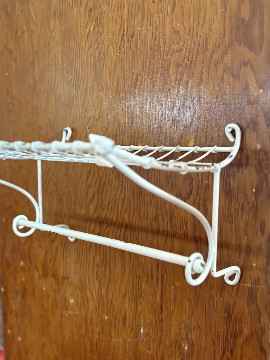 Off-white shabby chic metal wall rack with wire shelf and lower bar for storage and hanging.