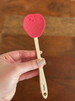 Red silicone strawberry spatula with wood handle, ideal for baking or kitchen prep.
