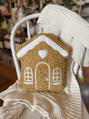 A front view of the gingerbread house pillow shows its white embroidered windows and snowy roof details.