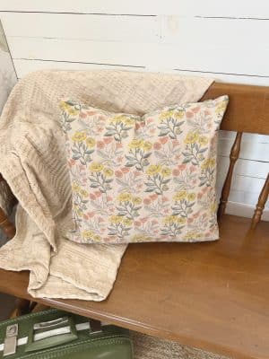 floral cotton pillow and neutral waffle throw blanket styled on a wooden bench