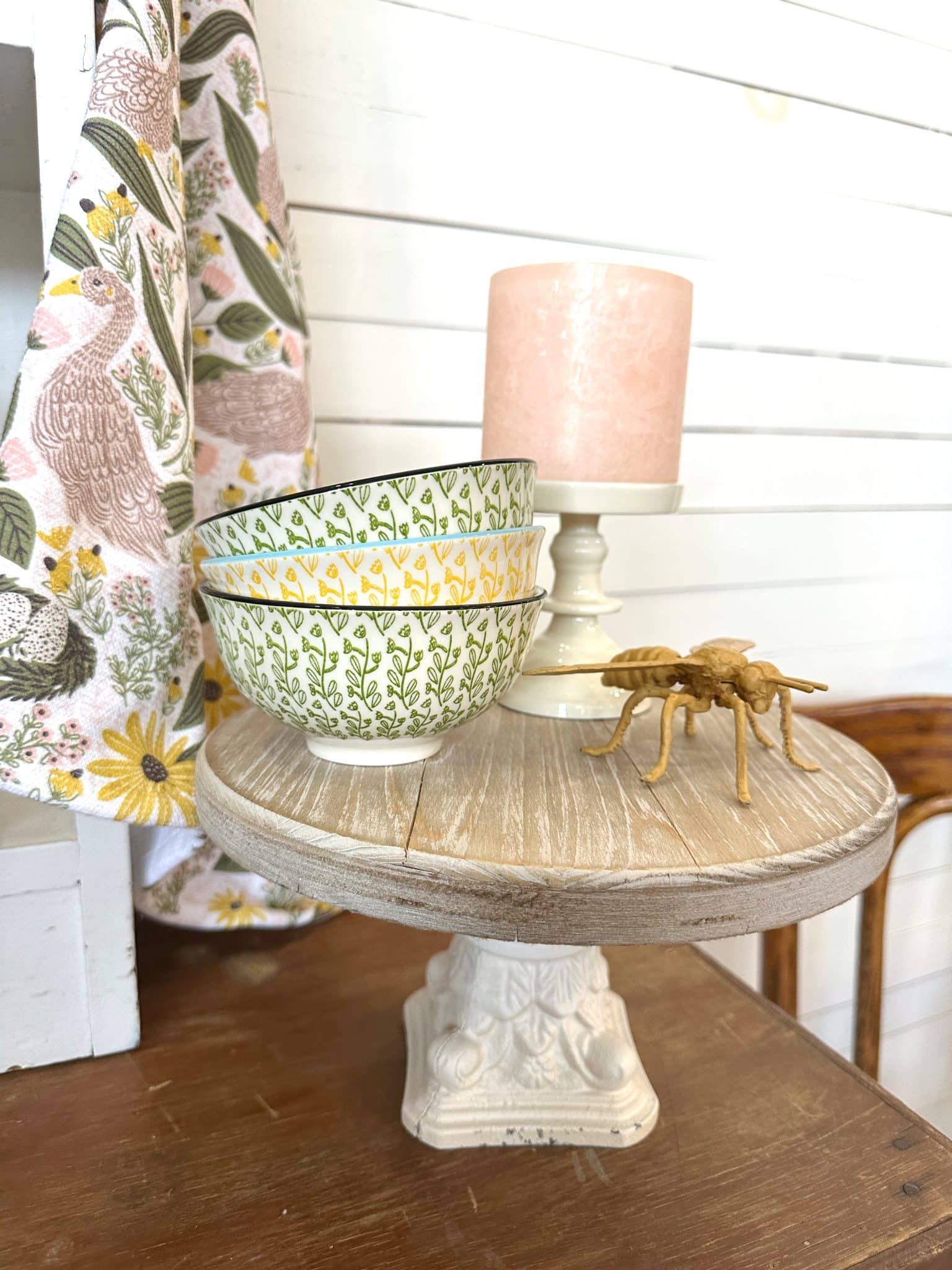 stacked yellow and green patterned stoneware bowls styled with a gold bee figurine and goose kitchen towel on rustic riser