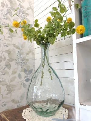 Large clear glass vase with a teardrop shape and bubbled texture, styled with faux greenery and yellow florals on a crochet doily.