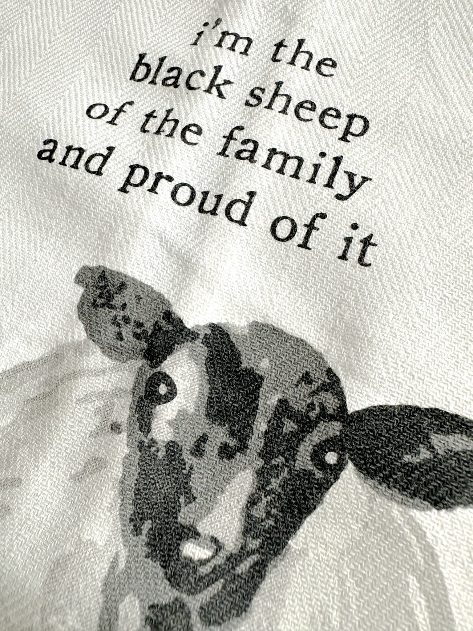 Close-up of a cotton tea towel with a black sheep illustration and the phrase “I’m the black sheep of the family and proud of it.”