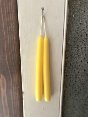 Pair of Sun Yellow taper candles hanging by their wicks against a rustic wood and white panel background.