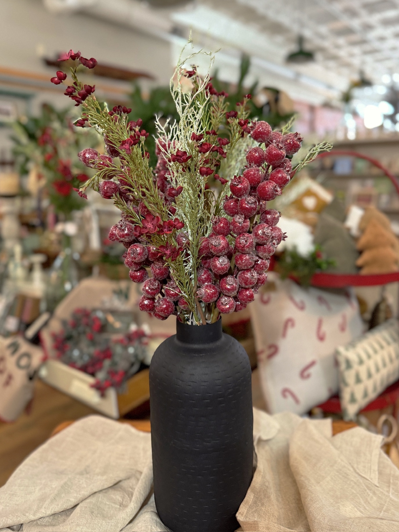 Textured black oblong vase filled with Glittered Red Berry Stems, Burgundy Waxflower Sprays, and Wispy Green Asparagus Sprays for a festive winter floral arrangement.