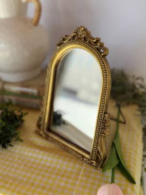 Front view of a beaded gold arched tabletop mirror with ornate detailing and easel back.