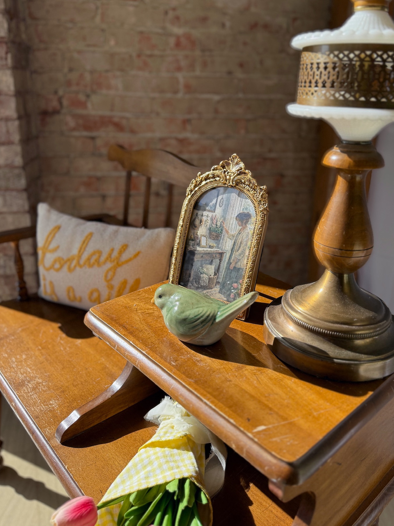 Arched gold photo frame and green bird figurine styled together on a wooden shelf with warm accents.