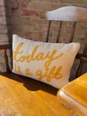 Today is a Gift embroidered lumbar pillow with mustard yellow lettering on a cream cotton cover, styled on a wooden chair for cozy cottage decor.