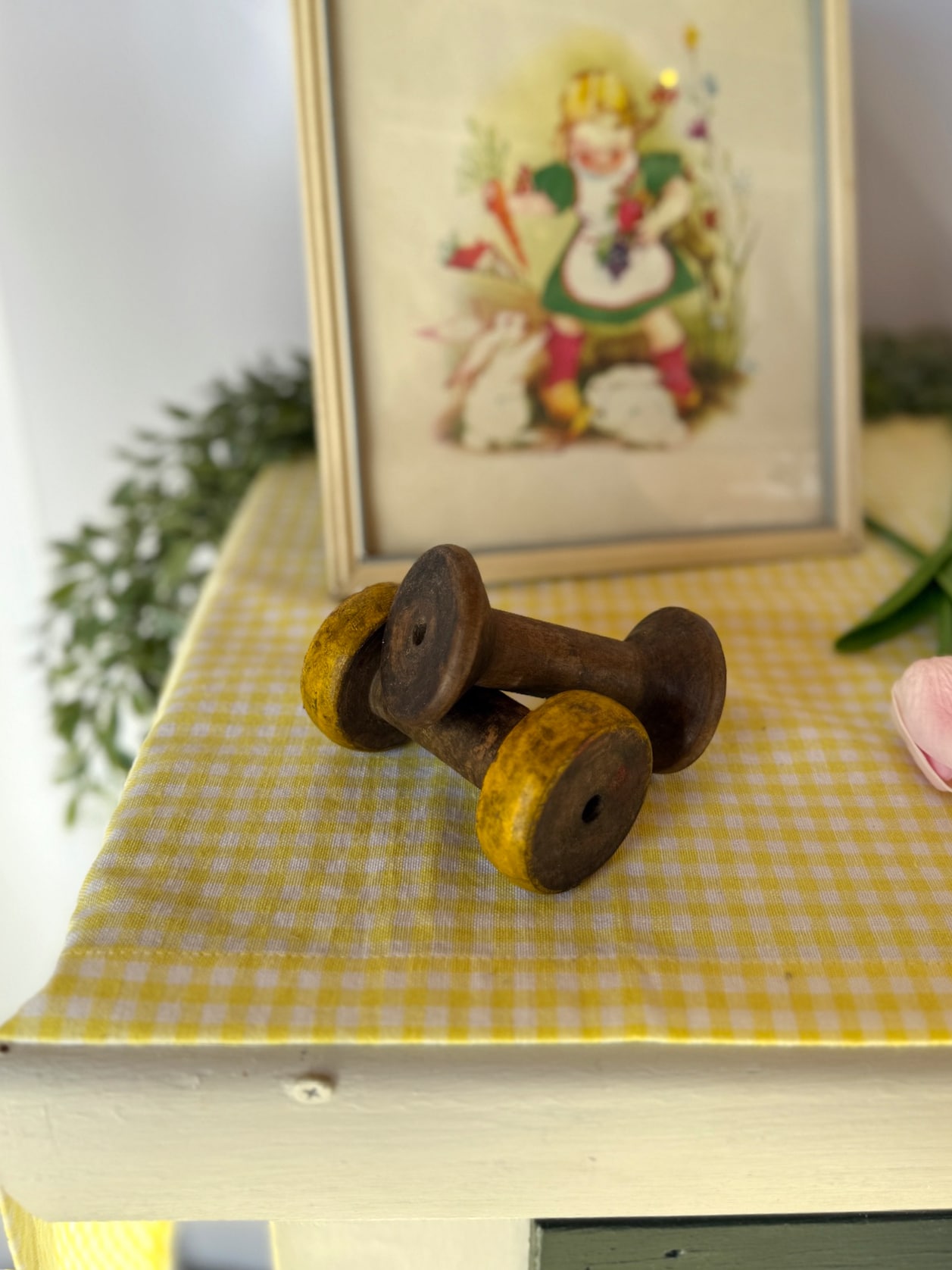 Vintage wooden spool handcrafted from reclaimed wood with a distressed finish, styled on a gingham surface with framed art for rustic decor.