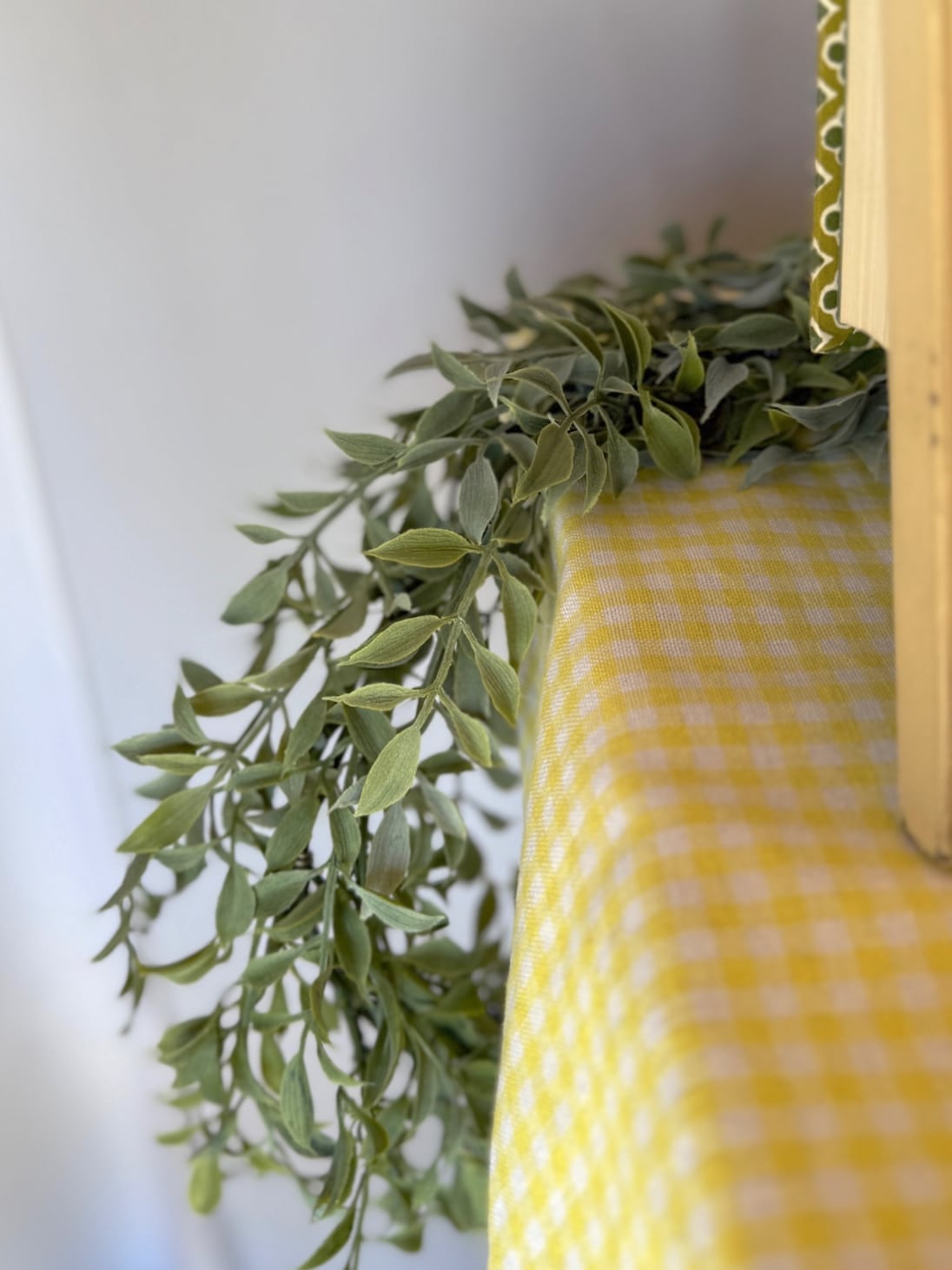 Soft green tea leaf garland draped over a cabinet with a yellow gingham runner.