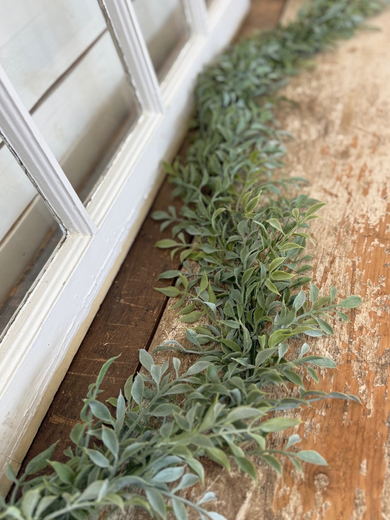 Tea leaf garland styled along a windowsill with layered soft green foliage.