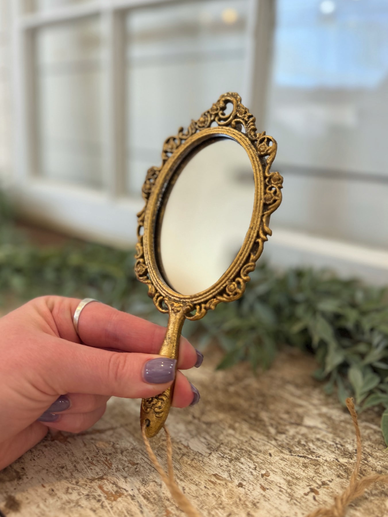 Ornate gold handheld mirror held upright showing scale and reflective surface.