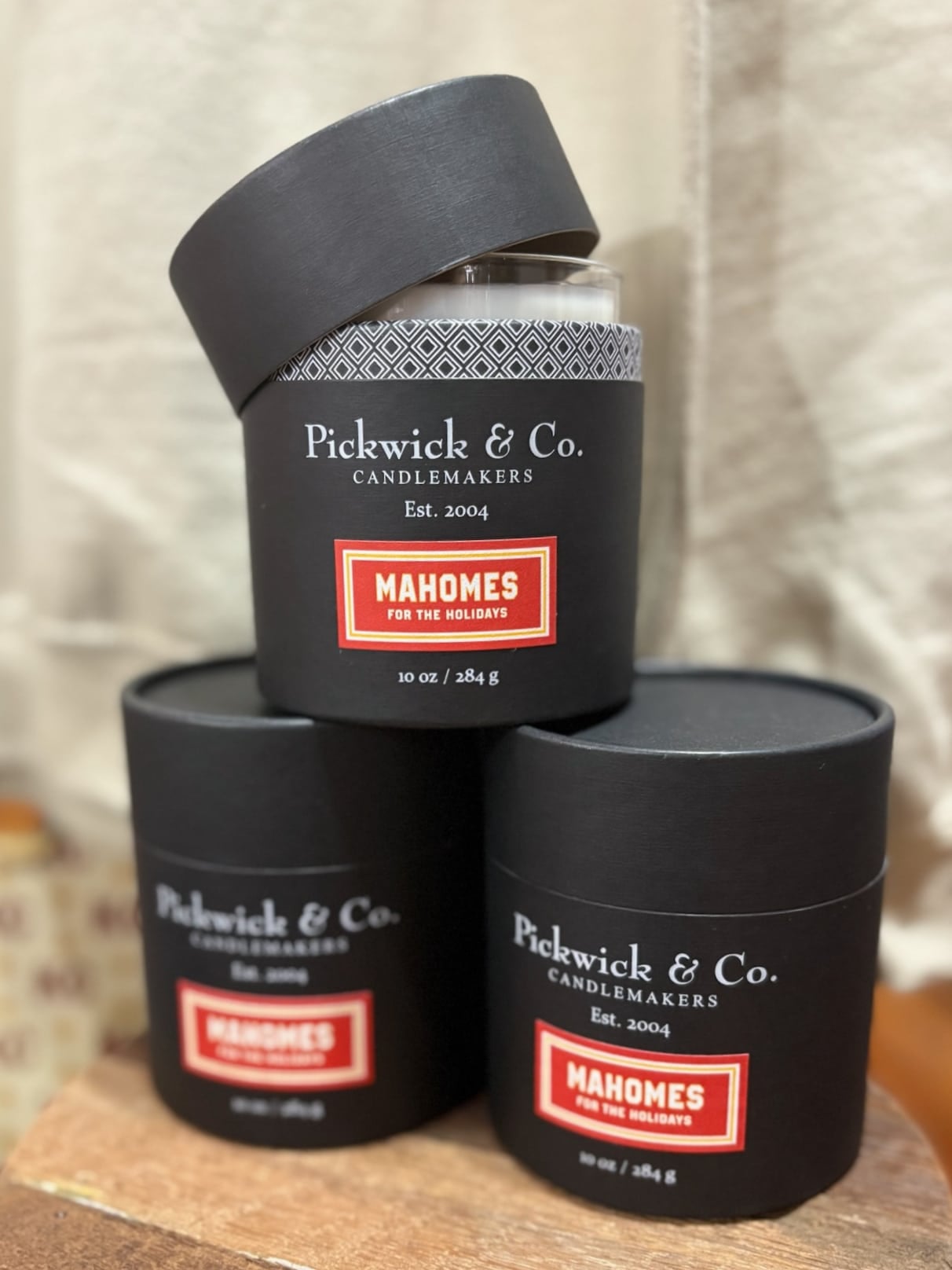 Pickwick & Co. Mahomes for the Holidays candle in a black gift box with the lid open, stacked among additional boxed candles.